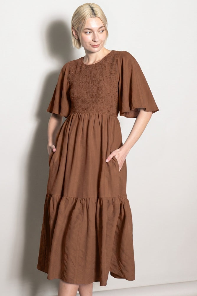 woman wearing a brown smocked waist midi dress with short flutter sleeves and side pockets