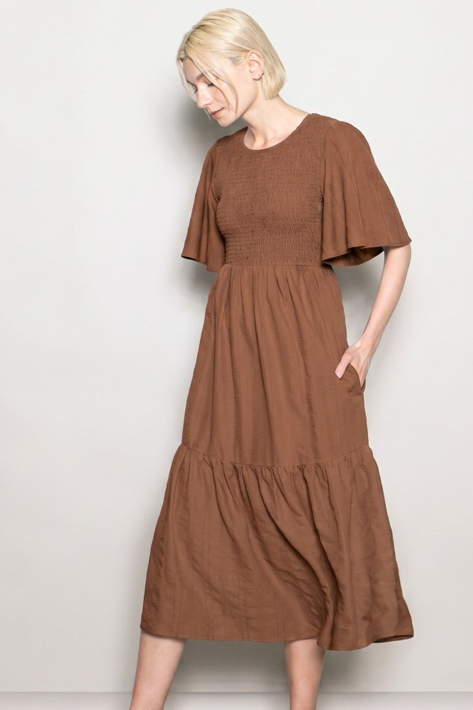 woman wearing a brown midi dress with smocked bodice and flared short sleeves, featuring a tiered skirt and pockets
