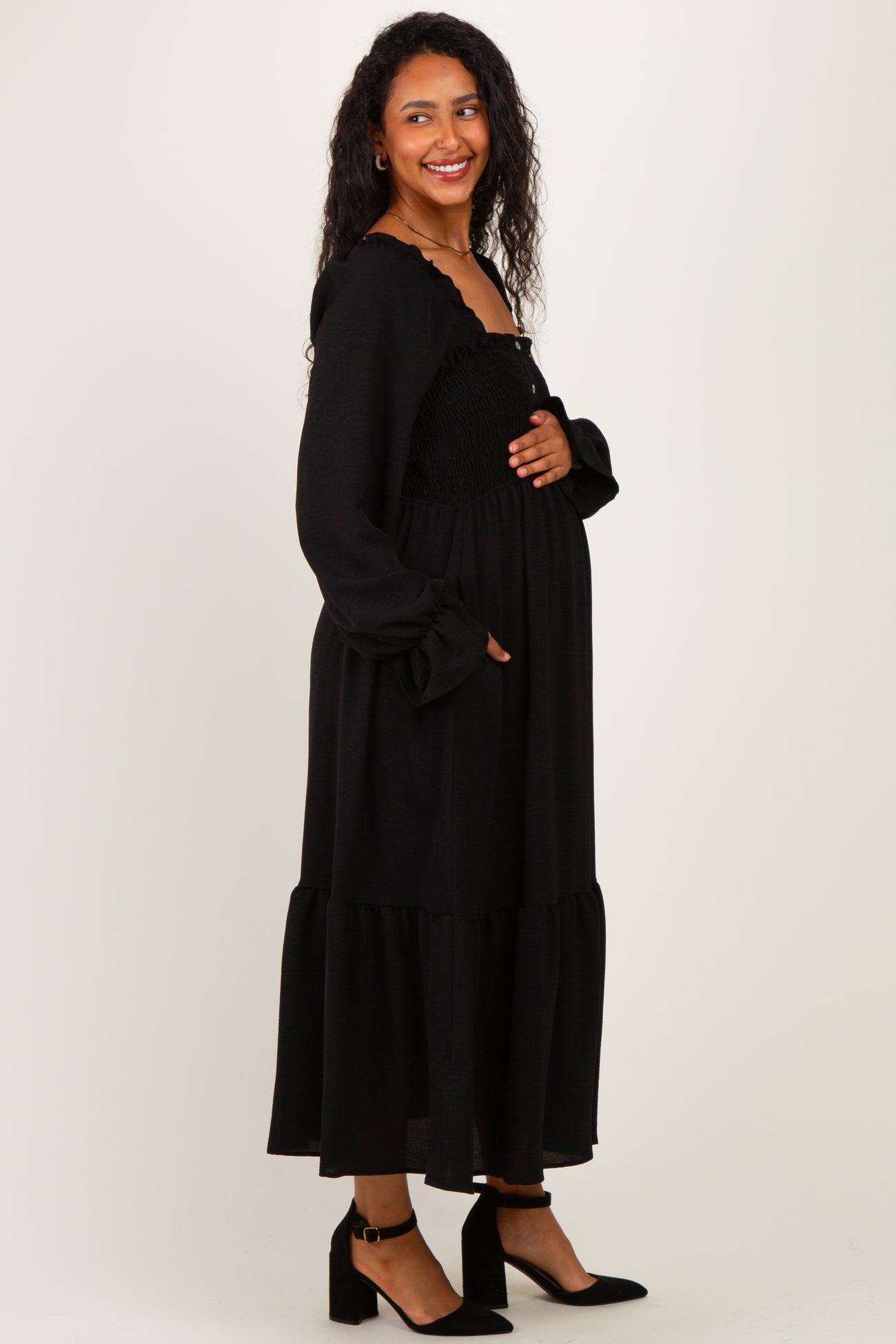 woman wearing a black maternity maxi dress with ruffled sleeves and a smocked bodice, holding her baby bump
