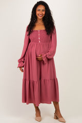woman wearing a mauve maternity dress with long sleeves, smocked bodice, and tiered skirt, holding her baby bump