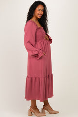 woman wearing a dusty rose long sleeve maternity dress with smocking and ruffled hem, showing her baby bump