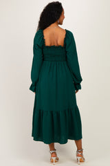 woman wearing a green maternity dress with a smocked bodice and long sleeves, showcasing a tiered skirt from the back
