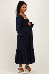 woman wearing a navy blue maternity dress with a smocked bodice and ruffled sleeves, holding her baby bump