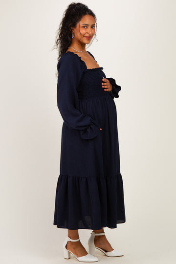 woman wearing a navy blue maternity dress with a smocked bodice and ruffled sleeves, holding her baby bump