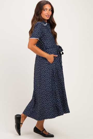 woman wearing a navy blue maternity dress with a floral print, short sleeves, and a tie waist detail