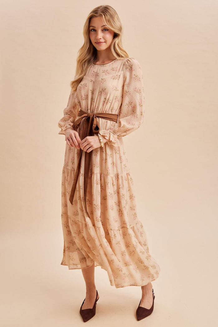 woman wearing a floral long sleeve maxi dress with a tie belt and flared hem, posing against a neutral background