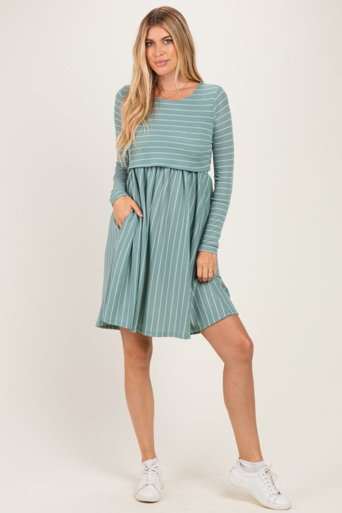 woman wearing a teal long sleeve striped dress with a fitted top and flared skirt, posing with one hand in the pocket