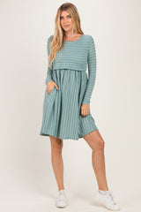 woman wearing a teal long sleeve striped dress with a fitted top and flared skirt, posing with one hand in the pocket