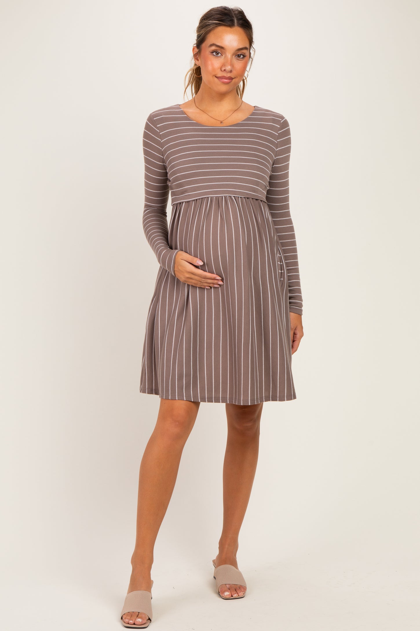 woman wearing a brown striped long sleeve maternity dress and holding her baby bump
