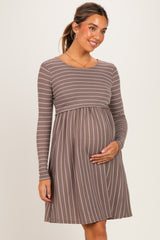 woman wearing a brown striped maternity dress with long sleeves and holding her baby bump