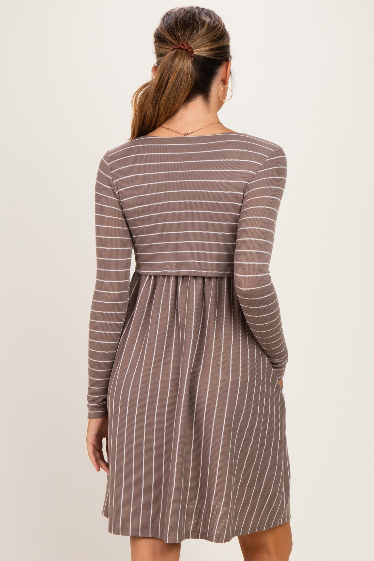 woman wearing a brown and white striped long sleeve maternity dress with a fitted bodice and flared skirt