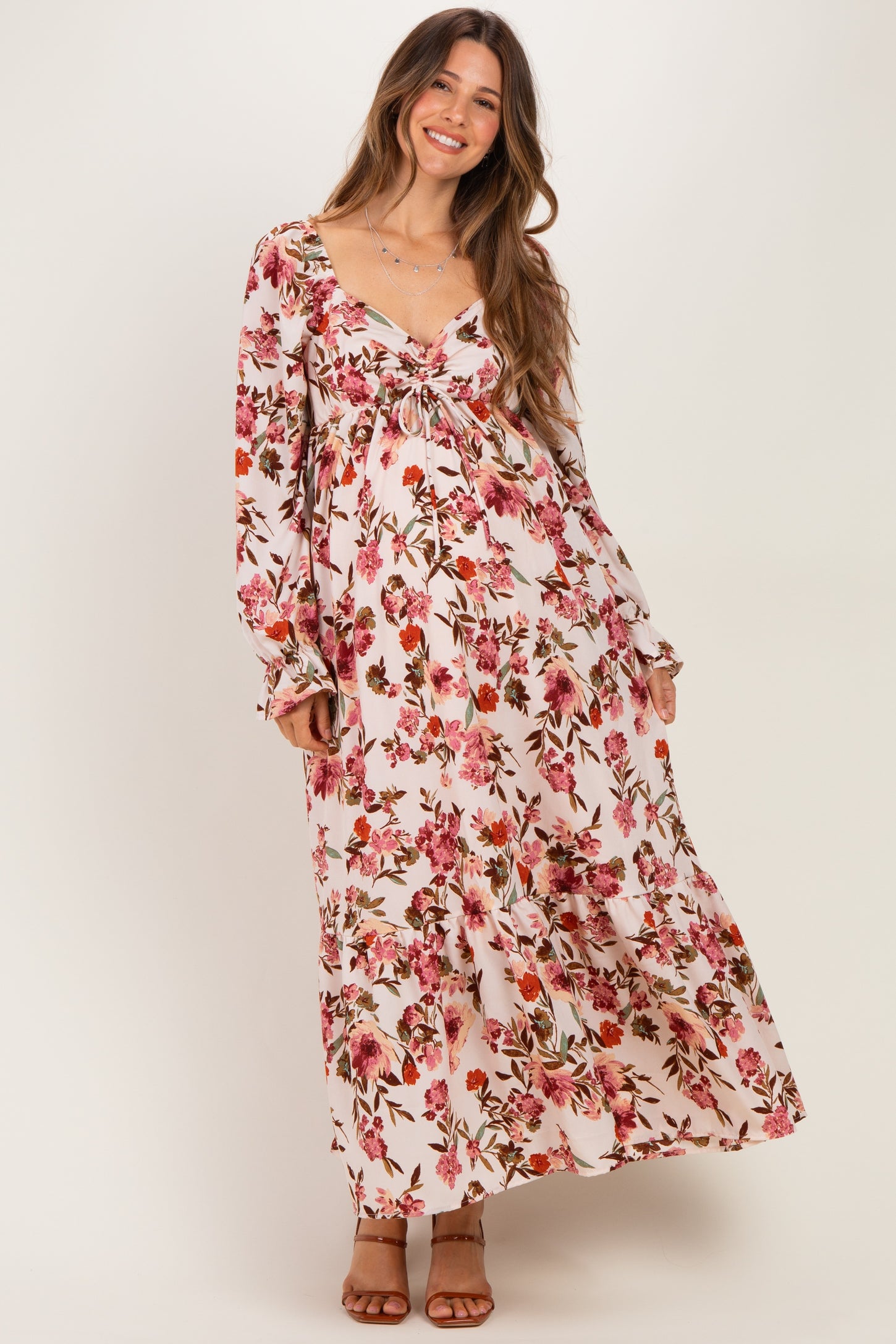 woman wearing a floral maxi maternity dress with a tie front and long sleeves, showcasing her baby bump