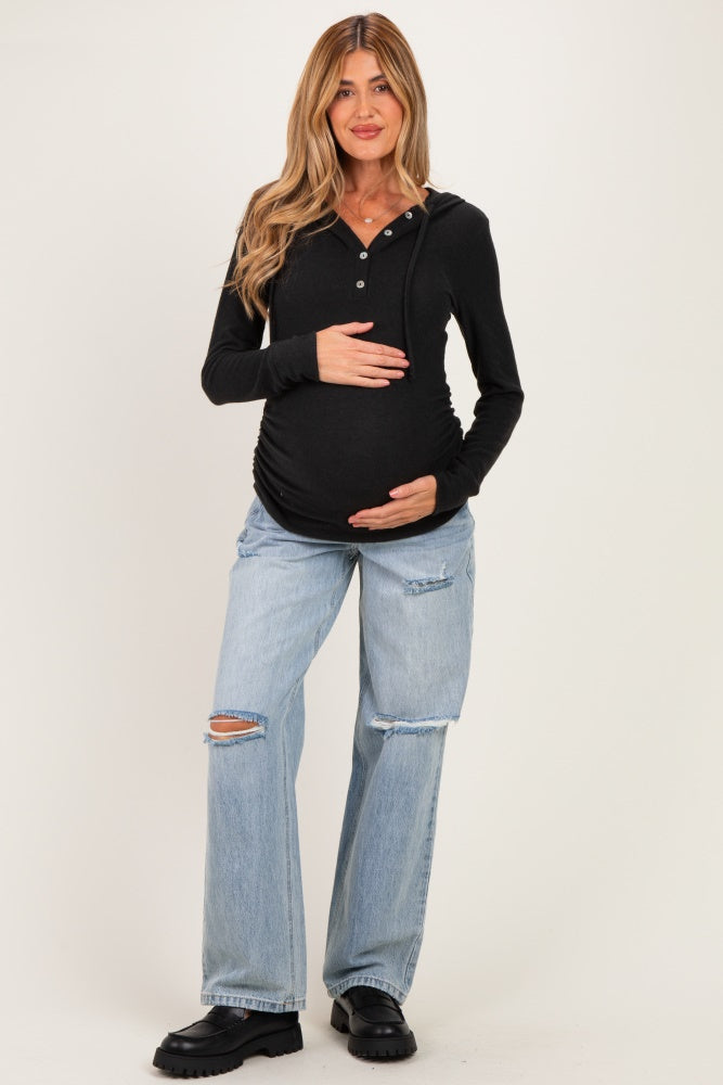 woman wearing a black long sleeve maternity hoodie with buttons and holding her baby bump, paired with distressed blue jeans