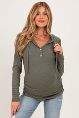 woman wearing a dark green maternity hoodie with a buttoned neckline and ruching at the sides, showcasing her baby bump