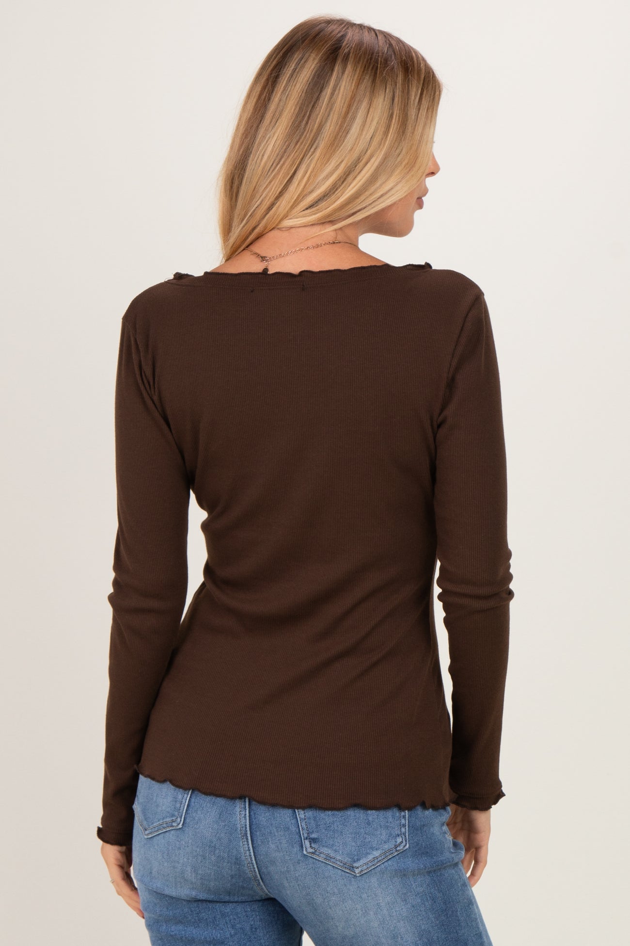 woman wearing a brown long sleeve top with a scalloped neckline and back view, paired with blue jeans