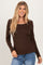 woman wearing a brown long sleeve top with a square neck and scalloped hem, smiling at the camera