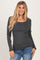 woman wearing a charcoal gray long sleeve top with a scalloped neckline and hem, paired with blue jeans