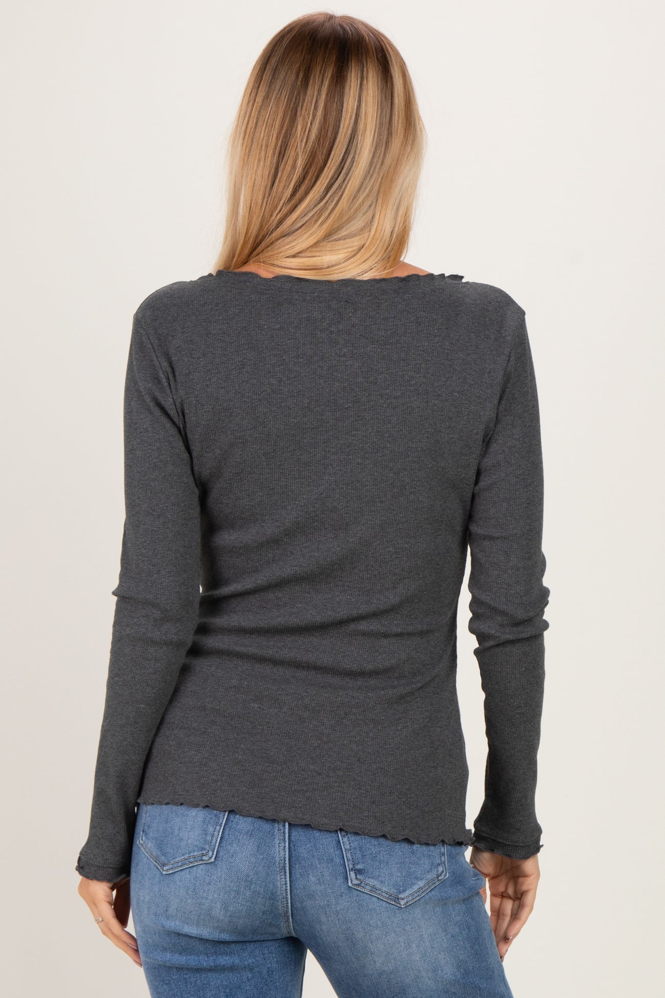 woman wearing a dark gray long sleeve top with a ruffled hem and back view, paired with blue jeans