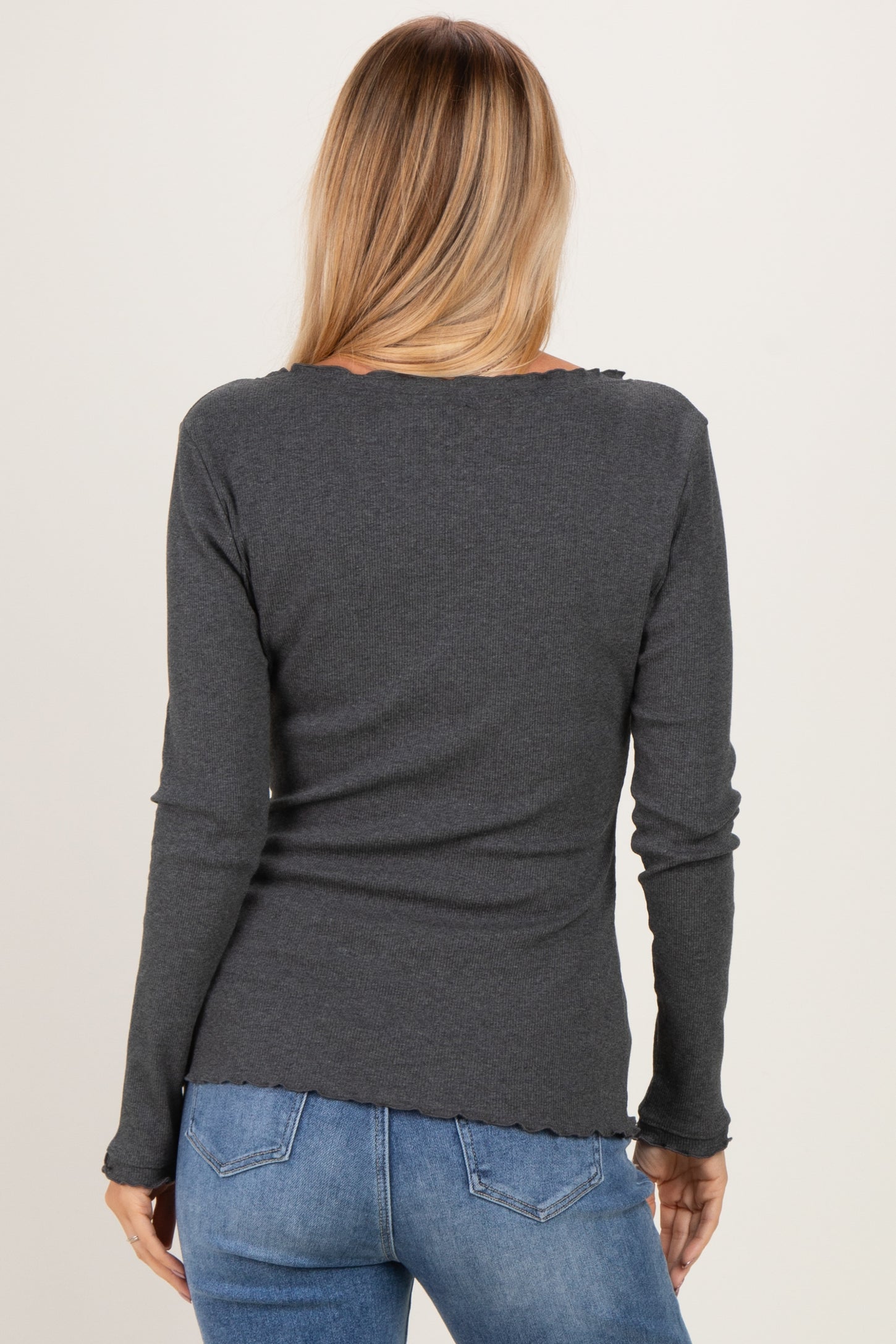 woman wearing a dark gray long sleeve top with a ruffled hem and back view, paired with blue jeans