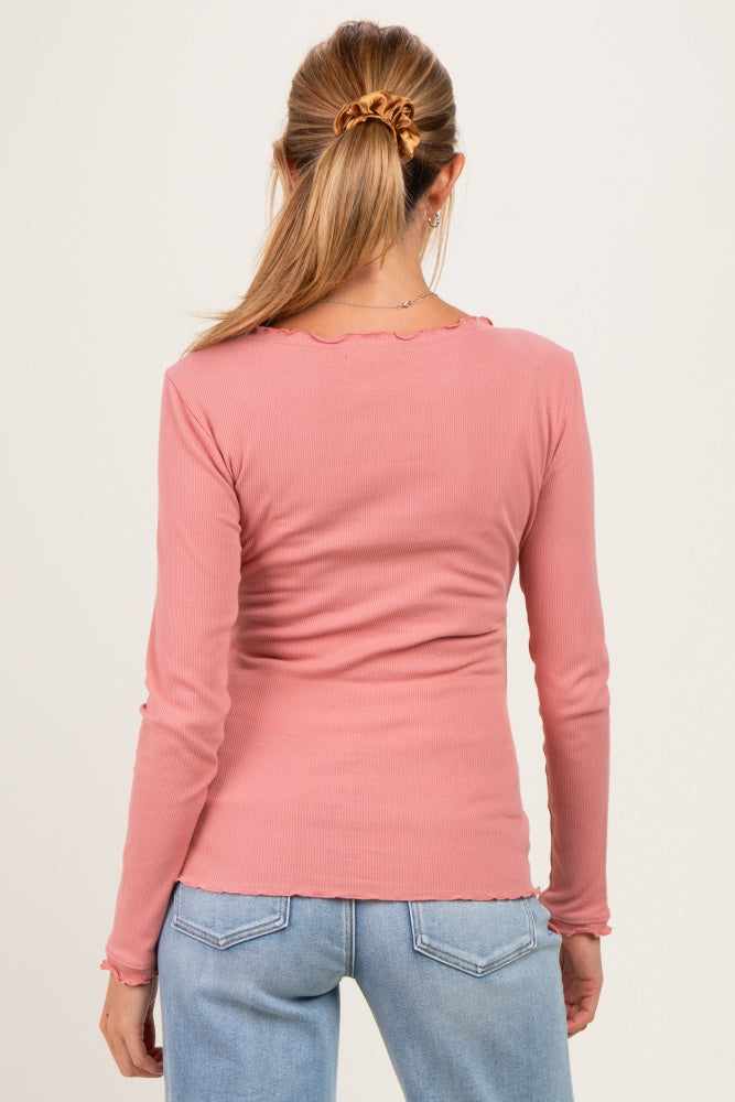 woman wearing a pink long sleeve maternity top with scalloped edges, seen from the back, paired with light blue jeans