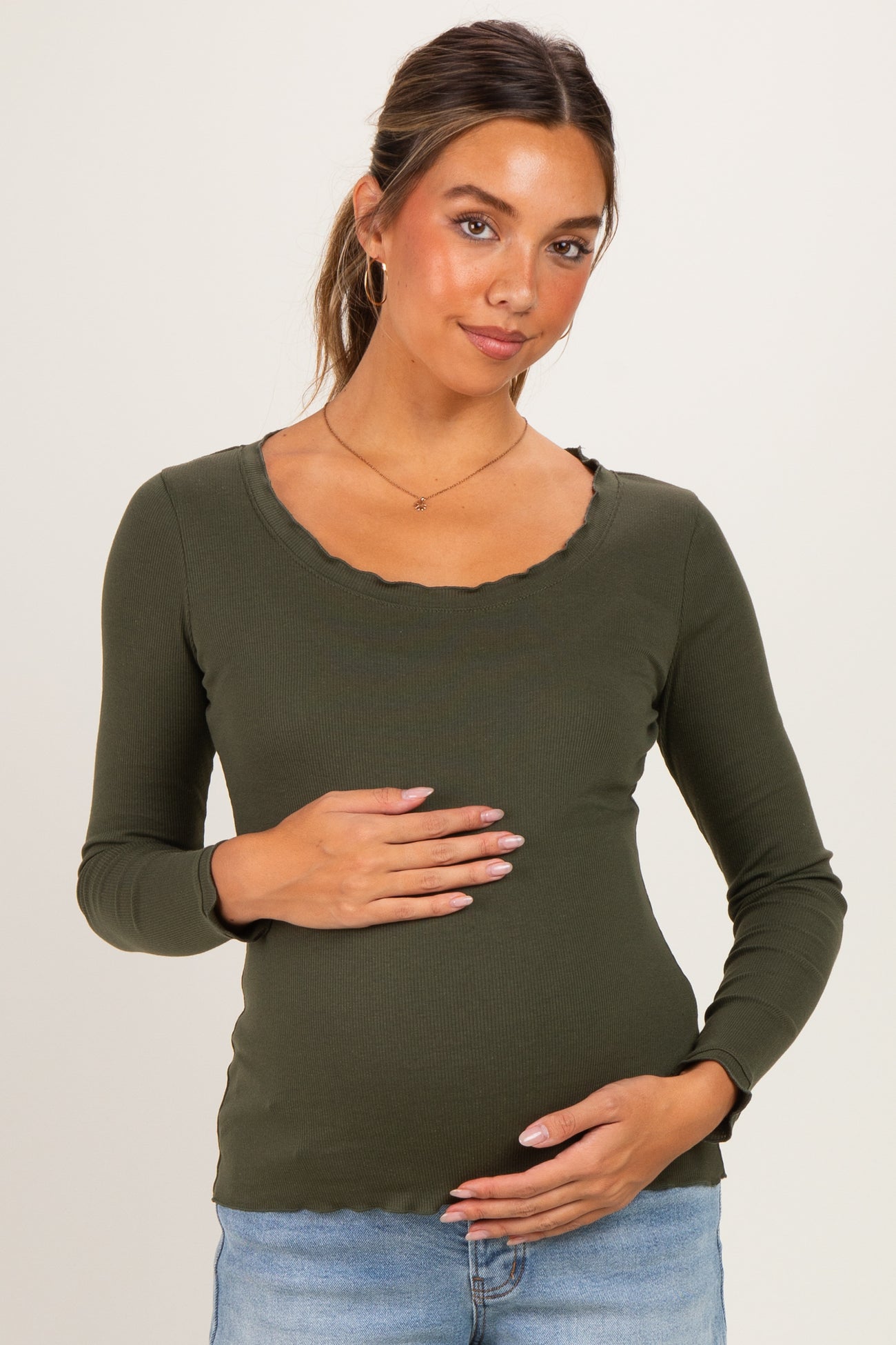 woman wearing an olive green long sleeve maternity top with a scalloped neckline and holding her baby bump