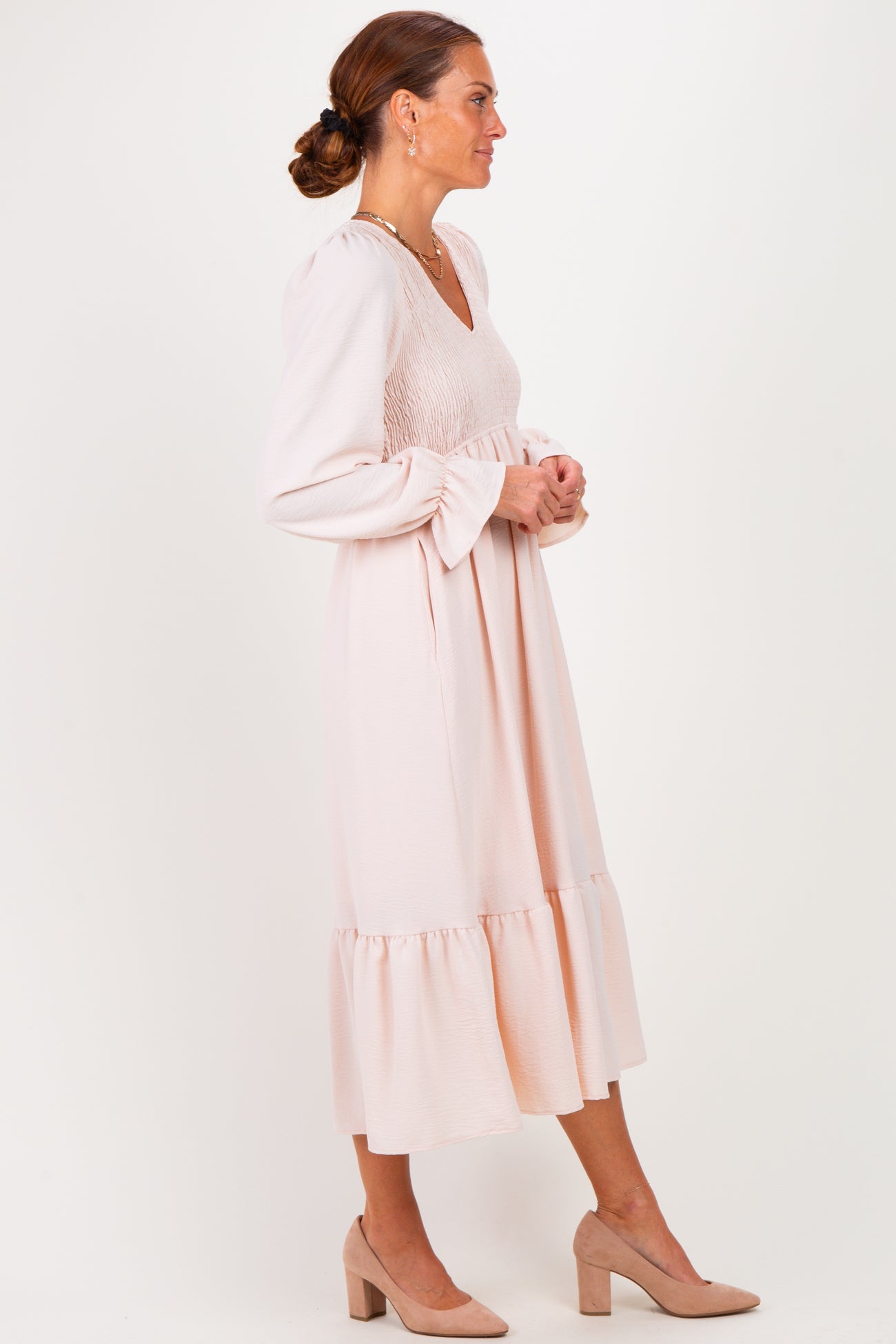 woman wearing a blush pink midi dress with a smocked bodice and flared sleeves, standing in profile with a ruffled hem