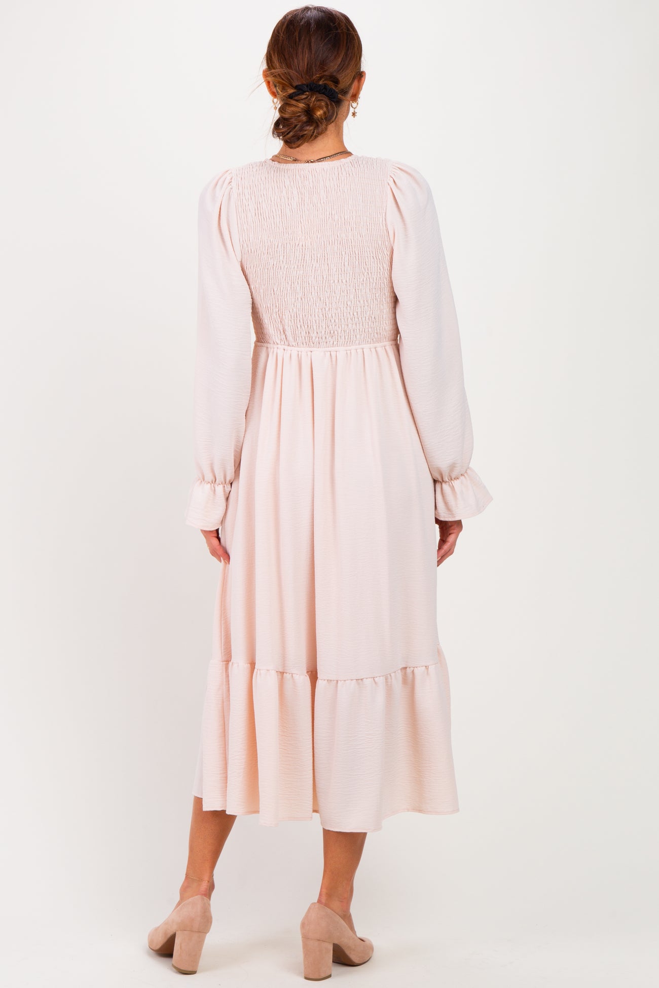 woman wearing a blush pink midi dress with smocked back and ruffled hem, viewed from the back