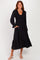 woman wearing a black long sleeve midi dress with smocked bodice and tiered hem, posing with hands in pockets