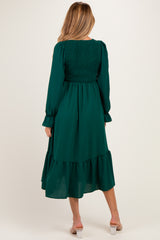 woman wearing a dark green maternity dress with smocked bodice and tiered hem, viewed from the back