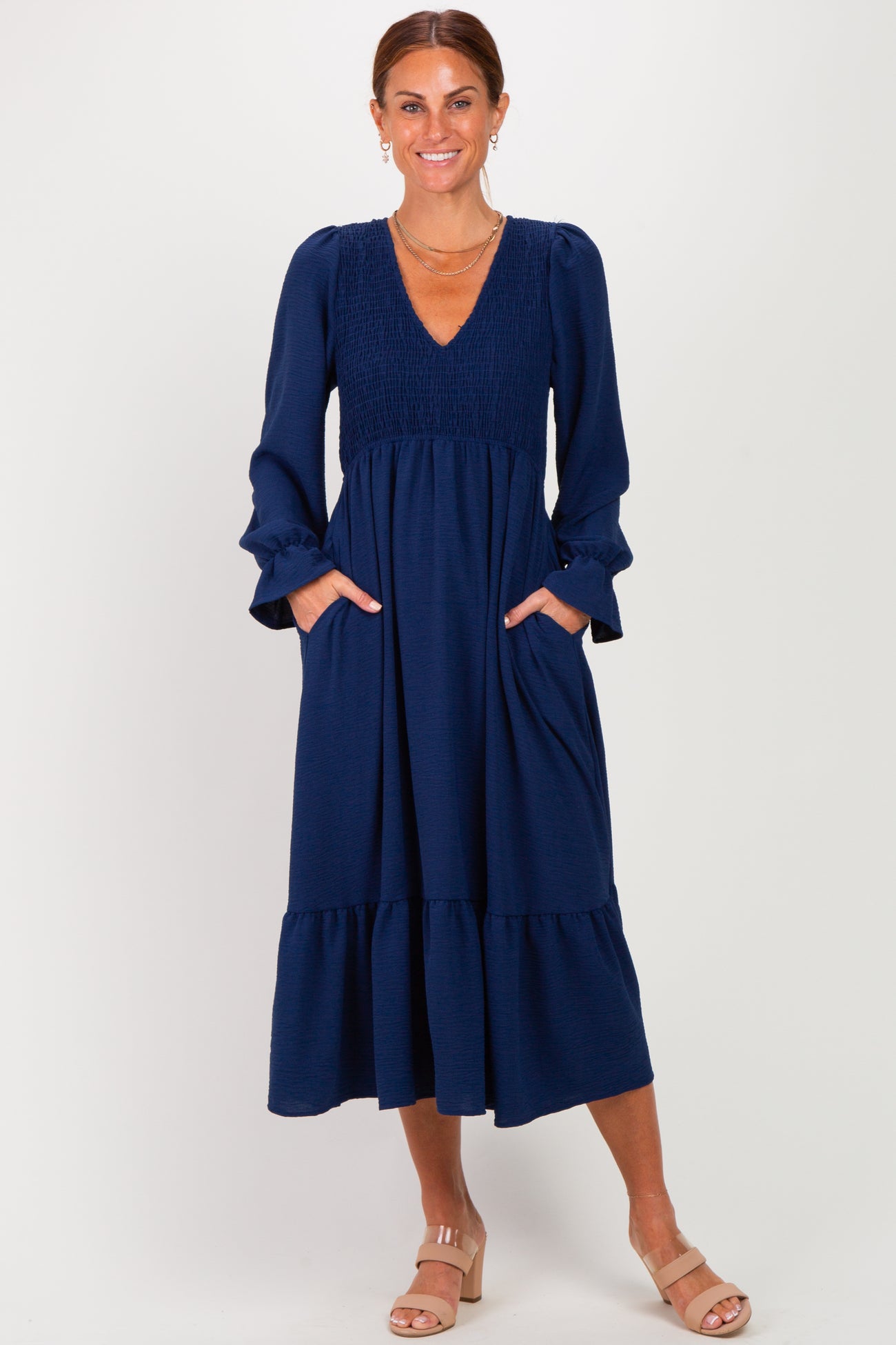 woman wearing a navy blue long sleeve maxi dress with smocked bodice and pockets, standing with hands in pockets