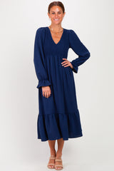 woman wearing a navy blue long sleeve tiered midi dress with a smocked bodice and ruffled hem, smiling at the camera