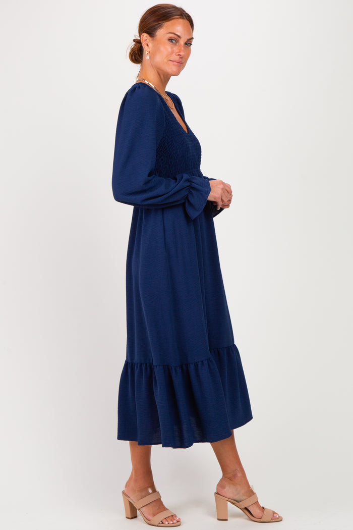 woman wearing a navy blue long sleeve dress with a smocked bodice and tiered ruffle hem, standing sideways