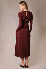 woman wearing a burgundy long sleeve midi dress with a keyhole back and gathered waist, viewed from the back