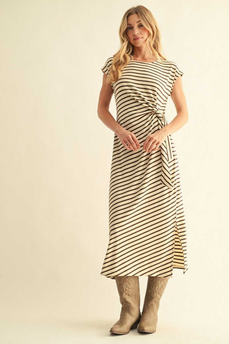 woman wearing a cream and black striped midi dress with a tie waist and high slit, paired with beige cowboy boots
