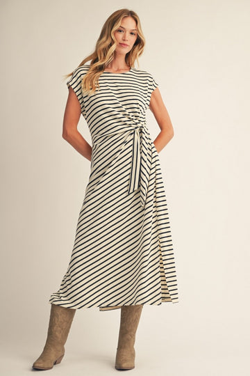 woman wearing a cream and black striped midi dress with a side tie and slit, paired with brown knee-high boots