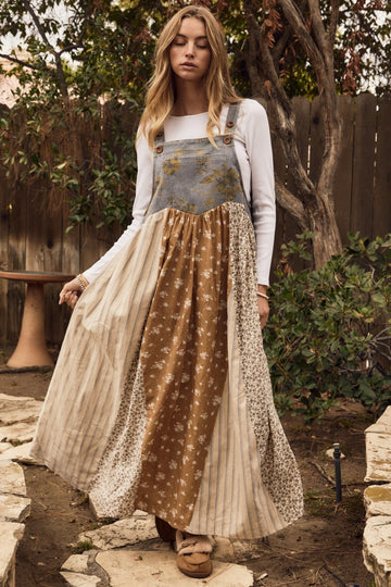 woman wearing a bohemian-style long patchwork dress with suspenders, featuring floral and striped patterns in earth tones