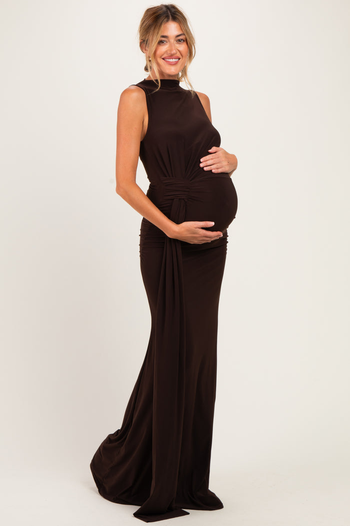 woman wearing a dark brown sleeveless maternity gown, posing and holding her baby bump
