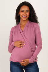 woman wearing a mauve wrap maternity top and holding her baby bump