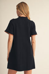 woman wearing a black short sleeve dress with scalloped detailing on the sleeves