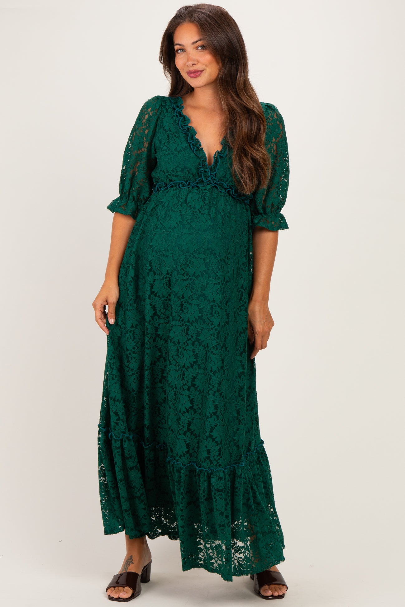 woman wearing a dark green lace maternity maxi dress with ruffled details and three-quarter sleeves, showing baby bump