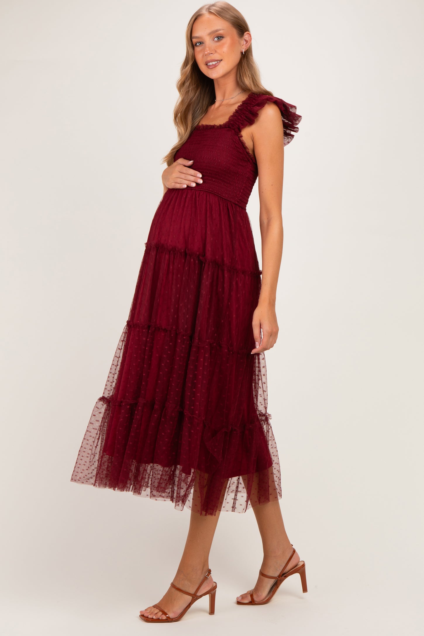 woman wearing a burgundy maternity dress with ruffle straps and tiered tulle skirt, showcasing her baby bump