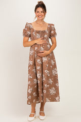 woman wearing a brown floral maternity dress with puff sleeves and a lace-up front, holding her baby bump