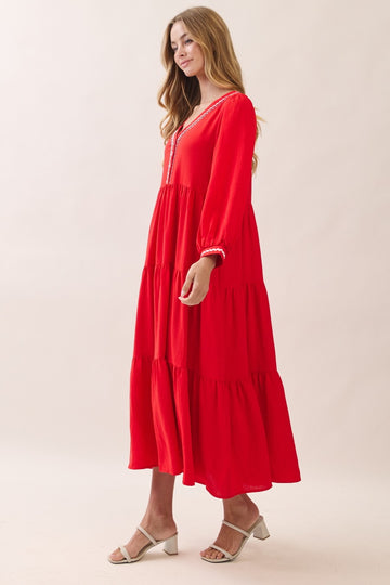 woman wearing a bright red tiered maxi dress with long sleeves and lace detailing, standing in profile