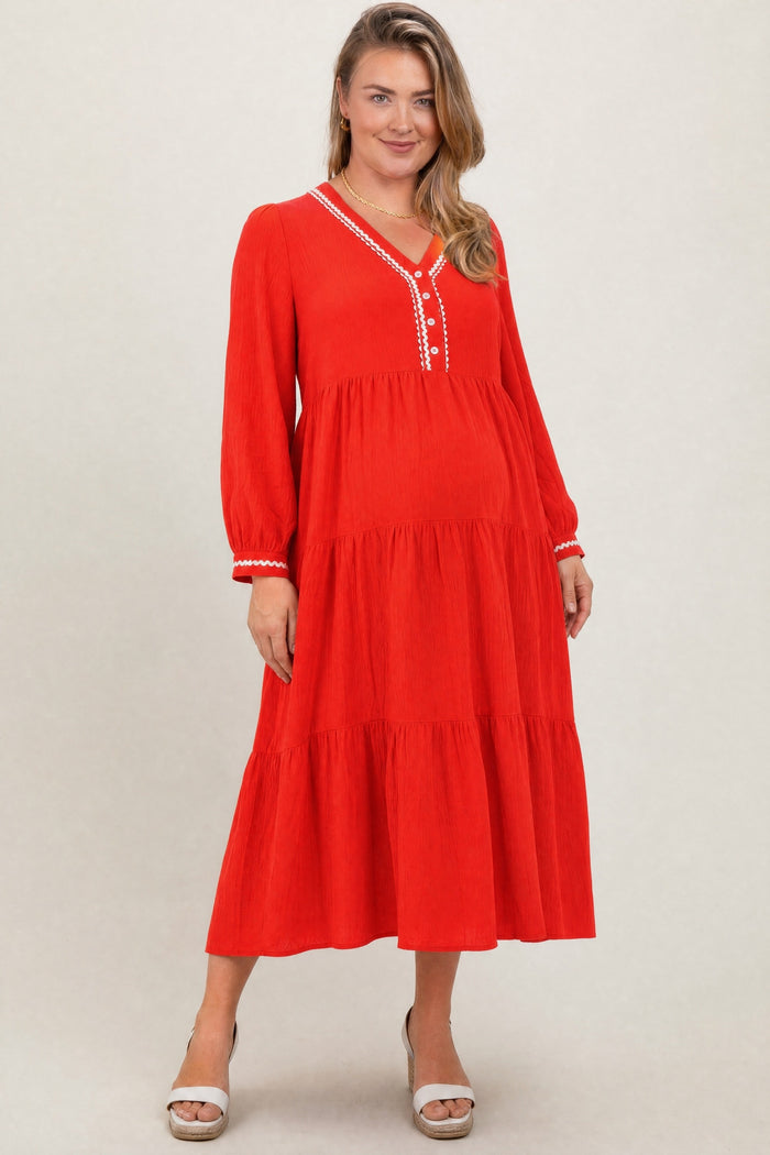 woman wearing a bright red maternity plus long sleeve tiered dress with button details and a visible baby bump
