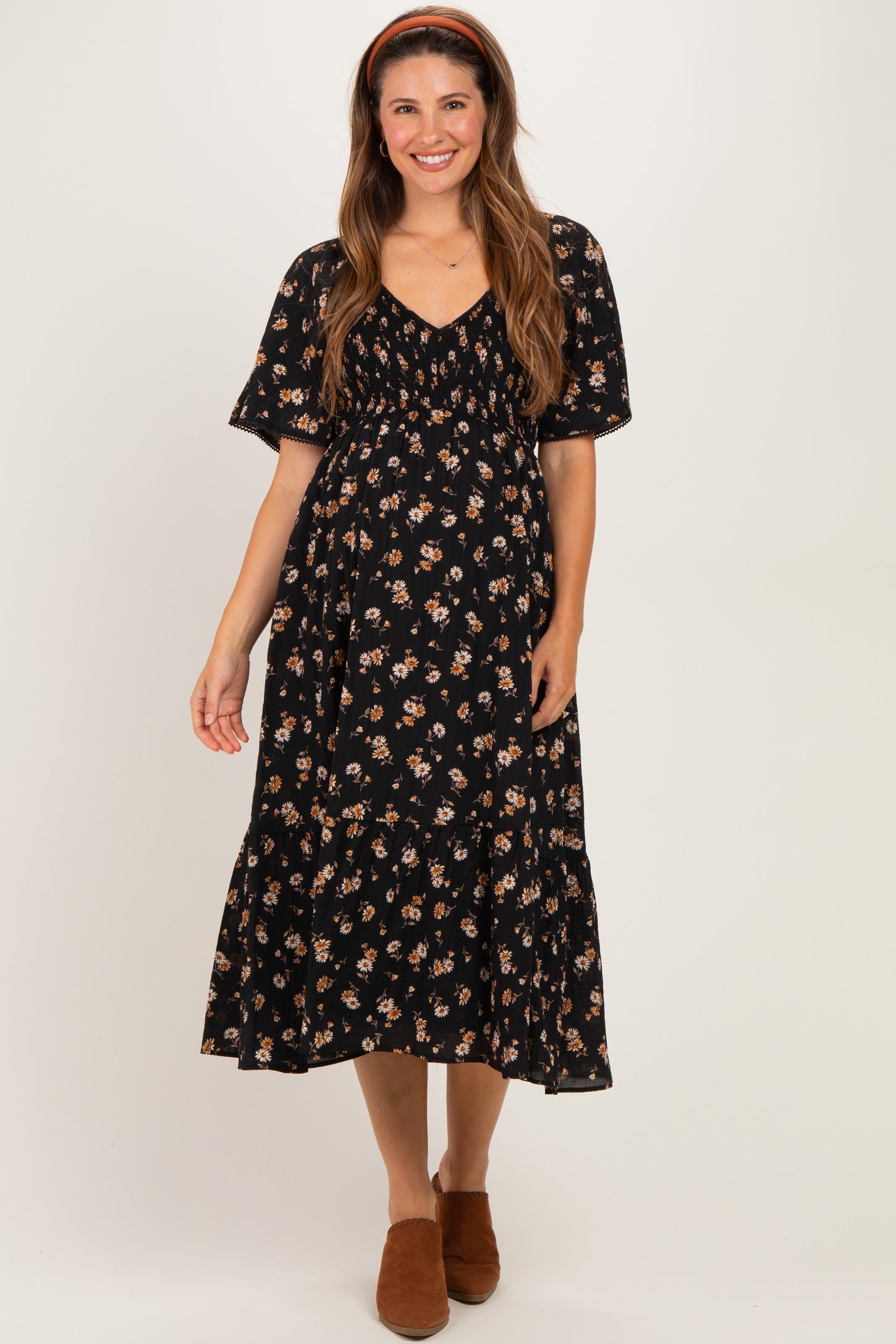 woman wearing a black floral maternity dress with short sleeves and a tiered skirt, smiling and standing with hands on her belly
