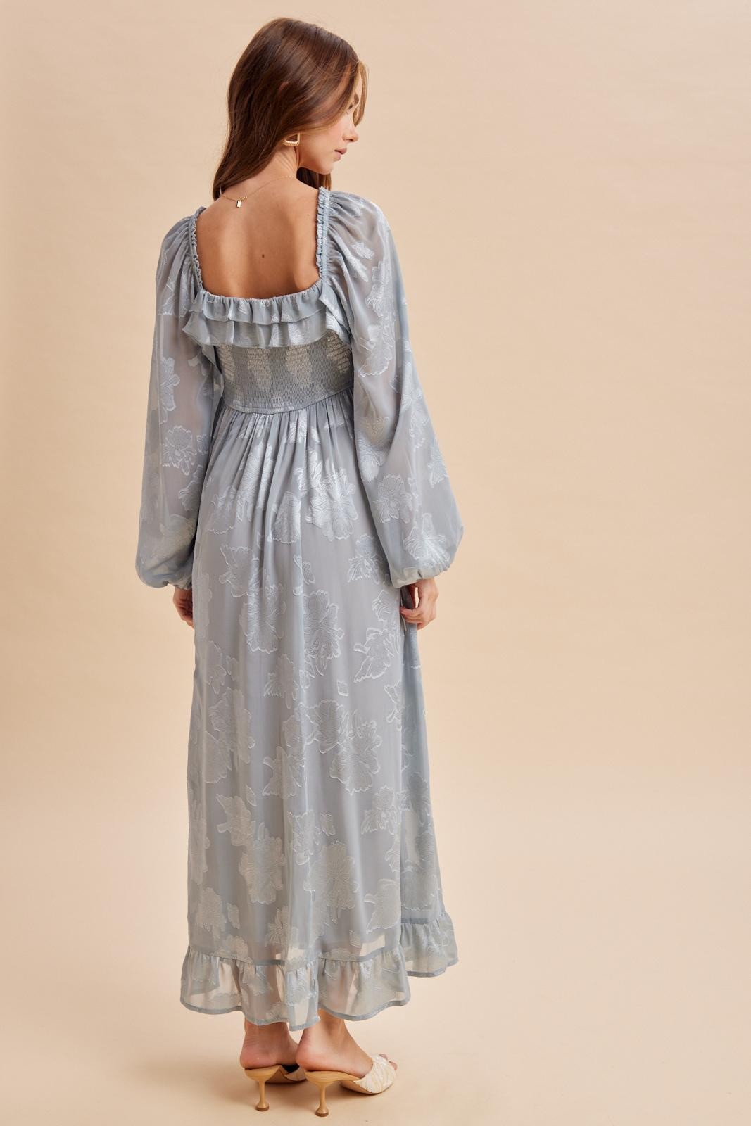woman wearing a light blue long sleeve maxi dress with floral patterns and puffed sleeves, showing the back view