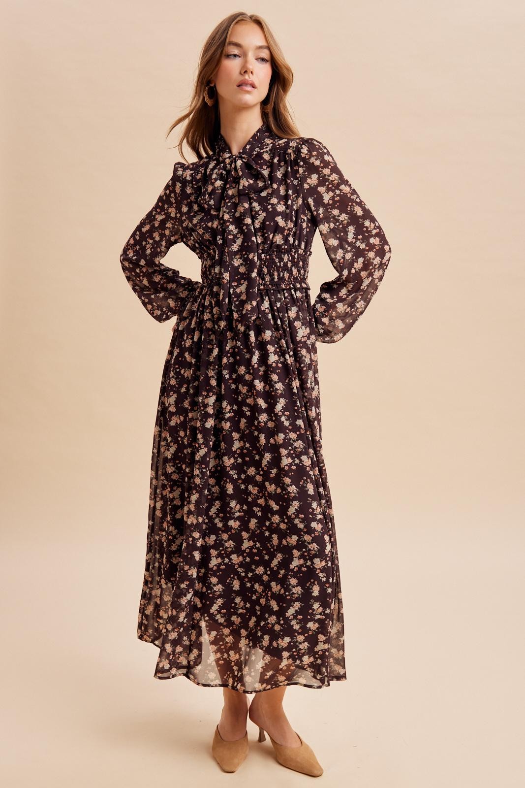 woman wearing a dark floral maxi dress with a bow tie neckline and long sleeves