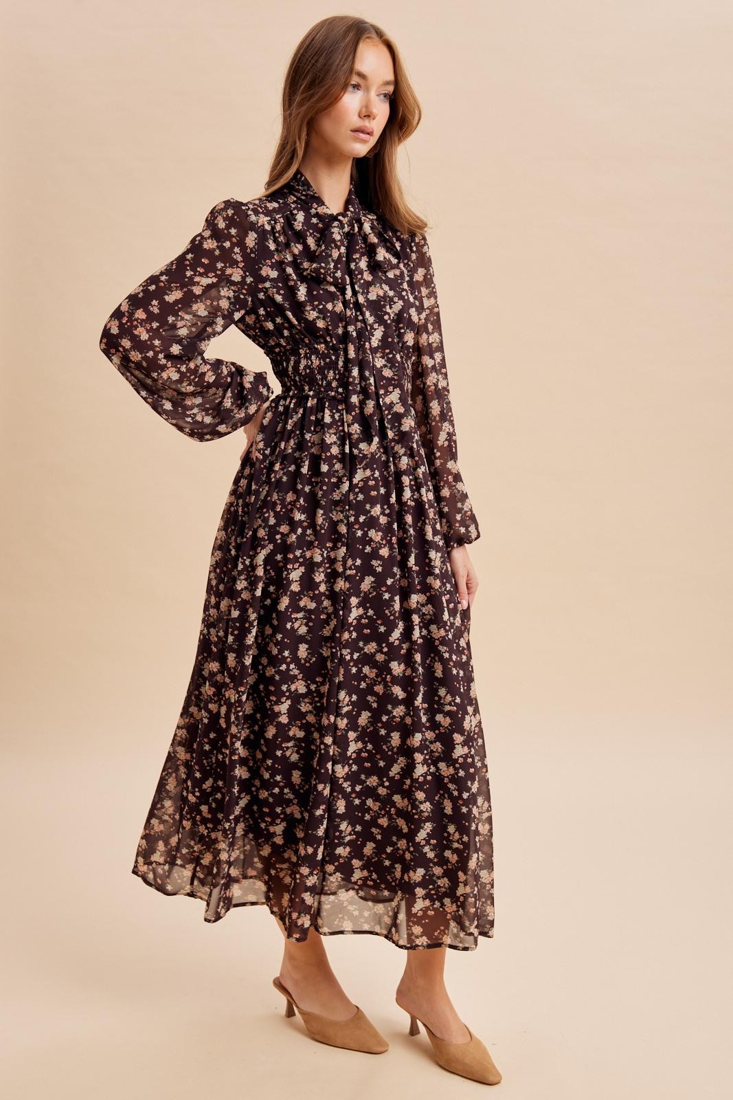 woman wearing a dark floral print maxi dress with long sleeves and a cinched waist, styled with nude heels