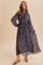 woman wearing a dark floral print long sleeve maxi dress with a tied neckline and sheer sleeves