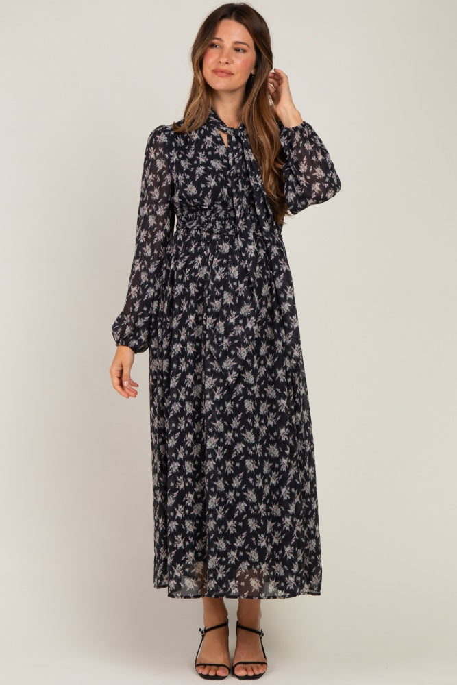 woman wearing a floral black maternity maxi dress with long sleeves and a tied neckline, showing her baby bump